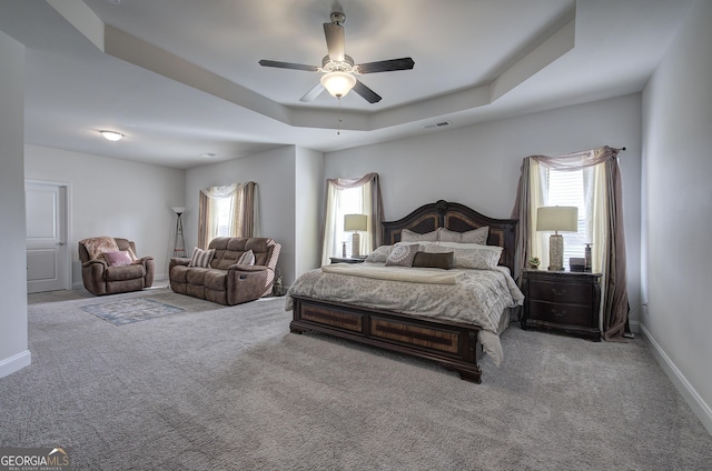 carpeted bedroom featuring multiple windows, ceiling fan, and a tray ceiling