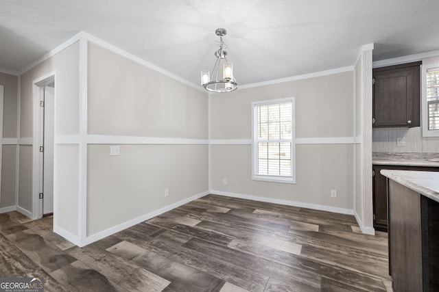 unfurnished dining area featuring dark hardwood / wood-style floors, ornamental molding, and a chandelier