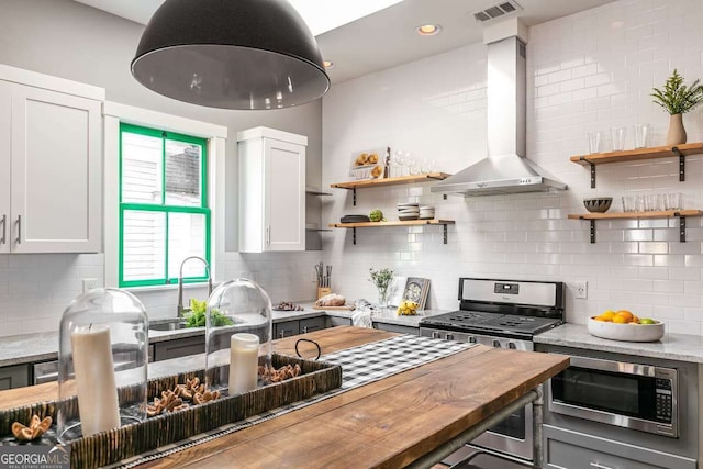 kitchen featuring white cabinetry, wooden counters, wall chimney range hood, and appliances with stainless steel finishes