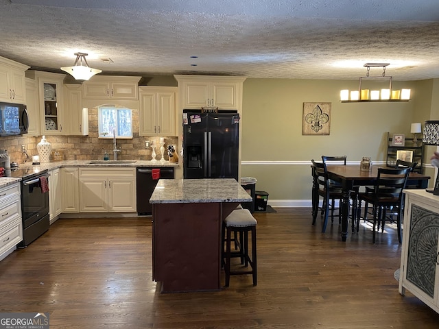 kitchen with a breakfast bar, sink, a center island, hanging light fixtures, and black appliances