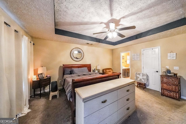 bedroom featuring ensuite bathroom, a textured ceiling, a tray ceiling, ceiling fan, and carpet