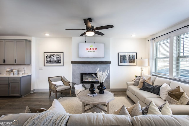 living room with a tile fireplace, ceiling fan, and dark wood-type flooring