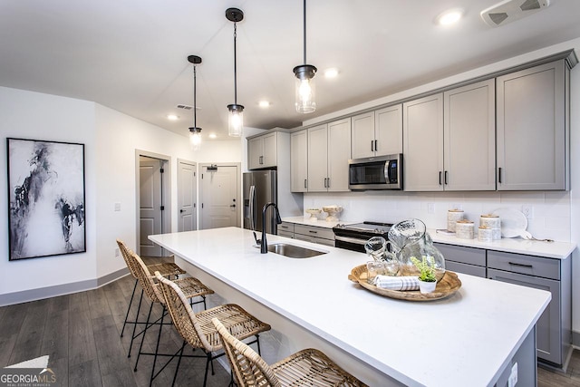 kitchen with pendant lighting, gray cabinetry, a center island with sink, sink, and stainless steel appliances