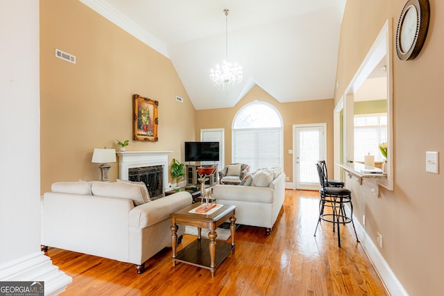 living room with hardwood / wood-style floors, high vaulted ceiling, an inviting chandelier, and ornamental molding