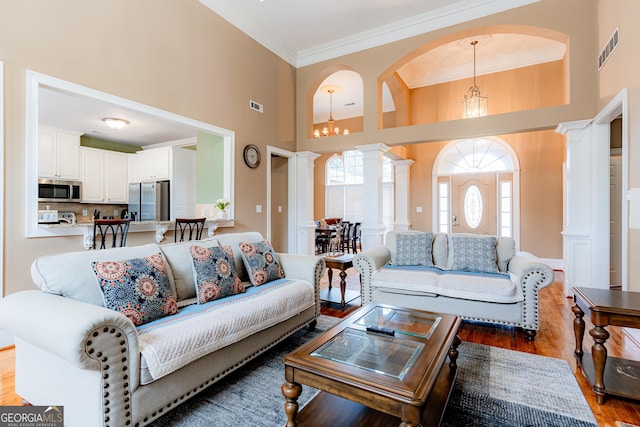 living room with a high ceiling, an inviting chandelier, decorative columns, light wood-type flooring, and ornamental molding