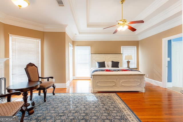 bedroom featuring light wood-type flooring, a tray ceiling, ceiling fan, and ornamental molding