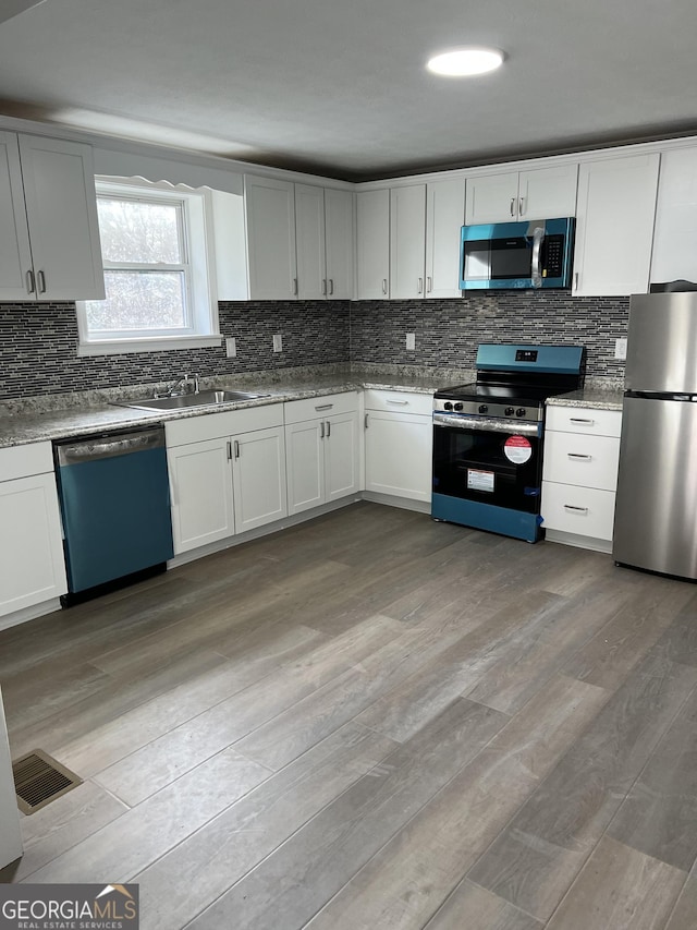 kitchen featuring white cabinetry, sink, light stone counters, light hardwood / wood-style flooring, and appliances with stainless steel finishes