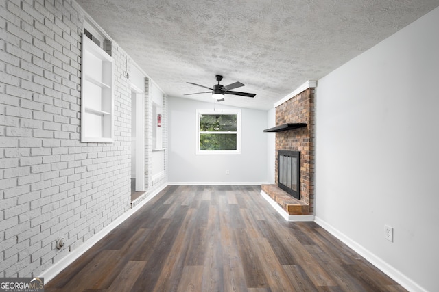 unfurnished living room featuring ceiling fan, dark wood-type flooring, brick wall, a textured ceiling, and a fireplace