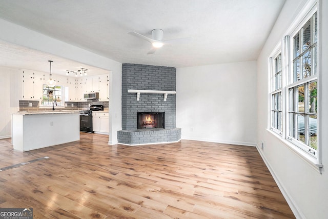 unfurnished living room featuring ceiling fan, sink, light wood-type flooring, and a fireplace