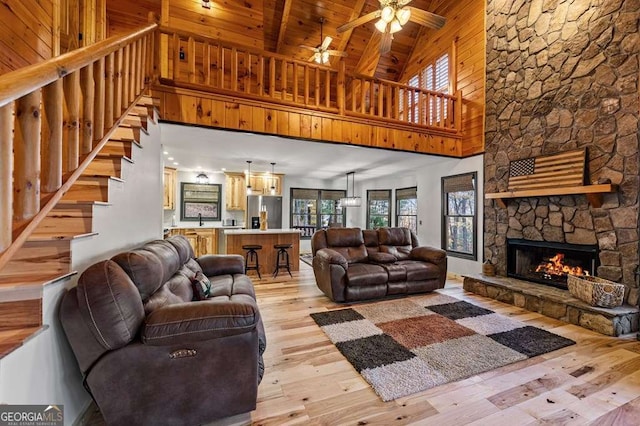 living room with light hardwood / wood-style flooring, ceiling fan, a stone fireplace, wooden ceiling, and beamed ceiling