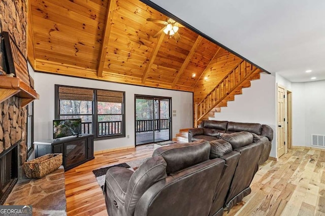 living room featuring a stone fireplace, high vaulted ceiling, light wood-type flooring, wood ceiling, and beam ceiling
