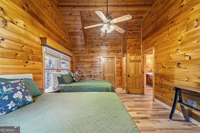 bedroom with ceiling fan, high vaulted ceiling, wooden walls, and light hardwood / wood-style floors