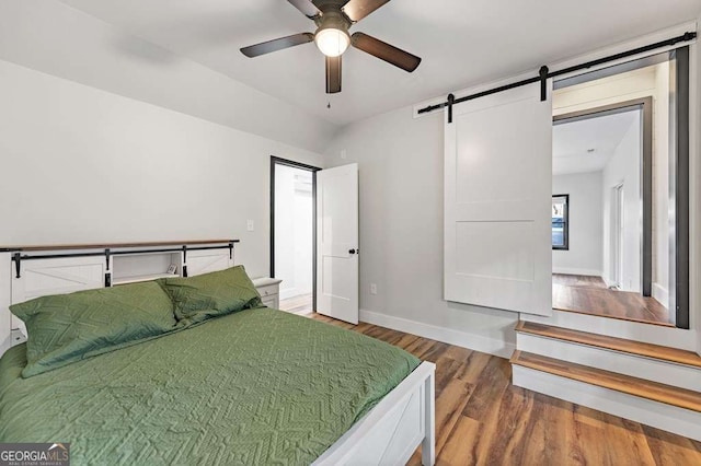bedroom with ceiling fan, a barn door, and hardwood / wood-style floors