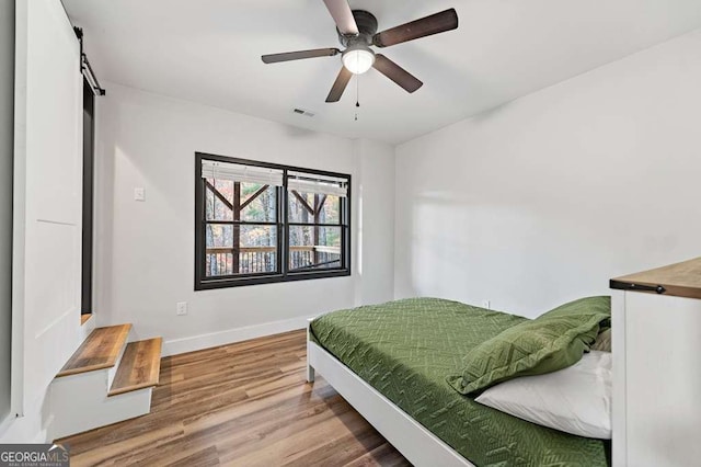 bedroom with wood-type flooring, a barn door, and ceiling fan