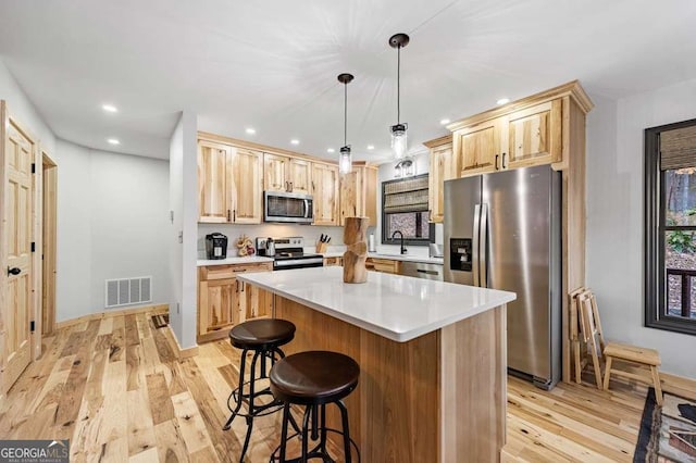 kitchen with pendant lighting, appliances with stainless steel finishes, a center island, light brown cabinetry, and light wood-type flooring