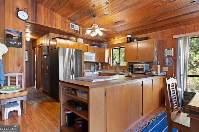 kitchen with kitchen peninsula, stainless steel fridge, vaulted ceiling, wooden walls, and light wood-type flooring