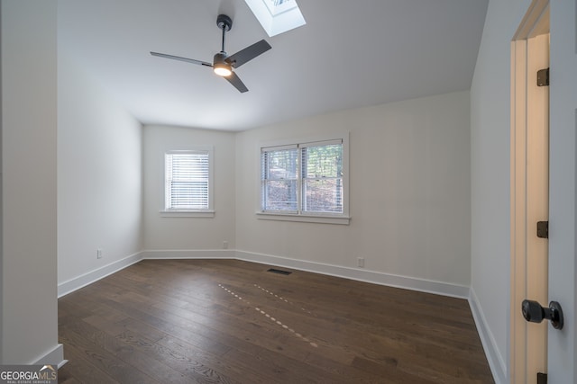 empty room featuring a skylight, ceiling fan, and dark wood-type flooring