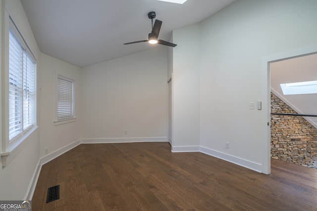 empty room featuring vaulted ceiling with skylight, ceiling fan, a healthy amount of sunlight, and dark wood-type flooring