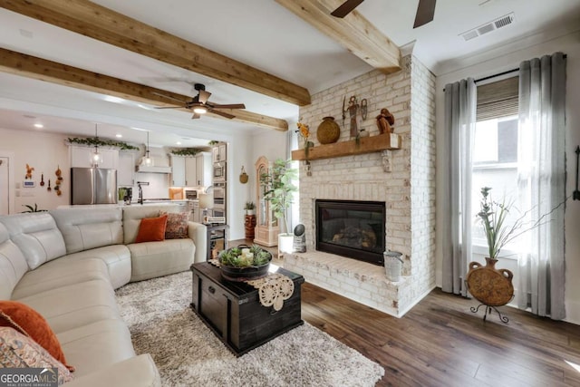 living room with beamed ceiling, a fireplace, ceiling fan, and dark wood-type flooring