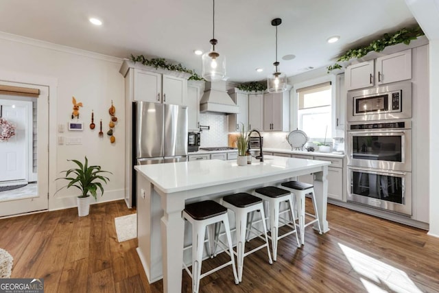 kitchen featuring an island with sink, stainless steel appliances, dark hardwood / wood-style floors, and custom exhaust hood