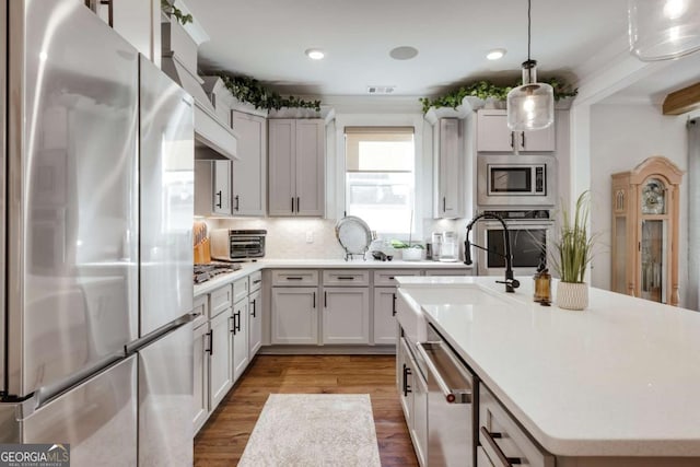 kitchen featuring hardwood / wood-style flooring, decorative backsplash, decorative light fixtures, a kitchen island, and stainless steel appliances