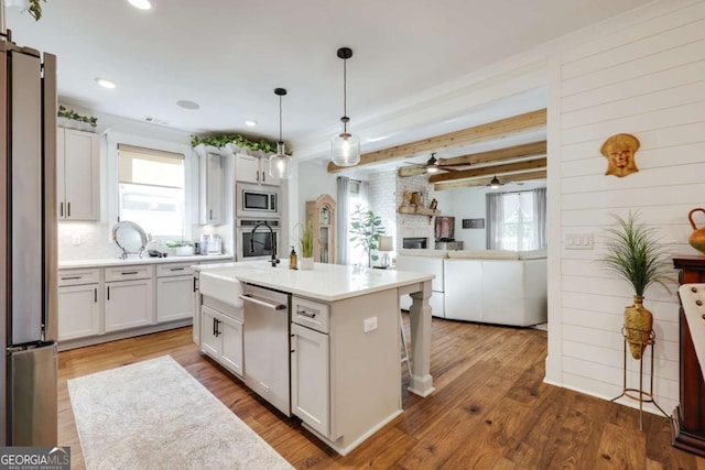 kitchen featuring beam ceiling, a center island with sink, white cabinetry, and stainless steel appliances