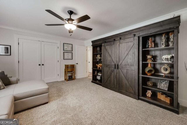 carpeted living room with ceiling fan, a barn door, and ornamental molding