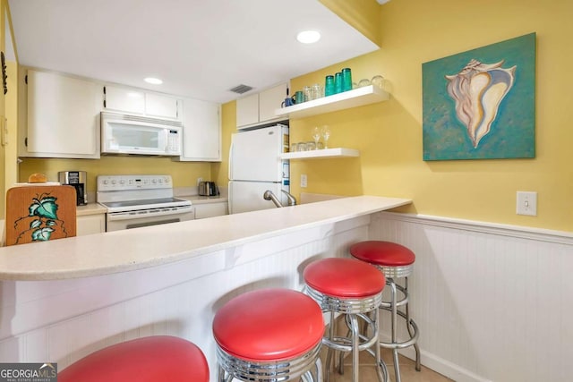 kitchen with a breakfast bar area, kitchen peninsula, white cabinets, and white appliances