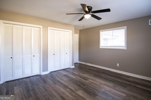 unfurnished bedroom featuring multiple closets, ceiling fan, and dark wood-type flooring