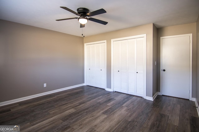 unfurnished bedroom with ceiling fan, dark wood-type flooring, and two closets