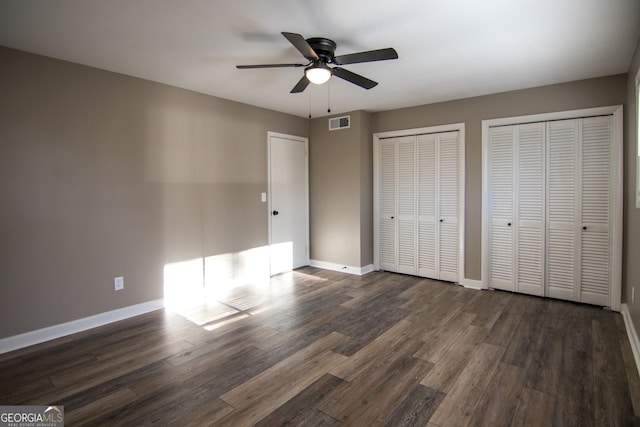 unfurnished bedroom with multiple closets, ceiling fan, and dark hardwood / wood-style floors