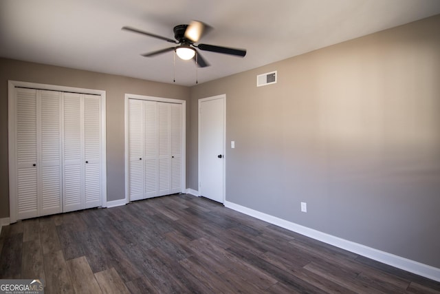 unfurnished bedroom with multiple closets, ceiling fan, and dark wood-type flooring