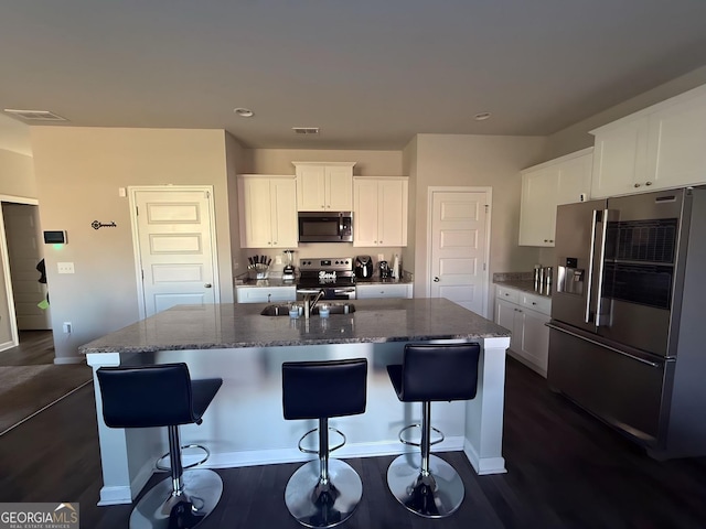 kitchen with dark wood-type flooring, a center island with sink, white cabinets, stone countertops, and stainless steel appliances