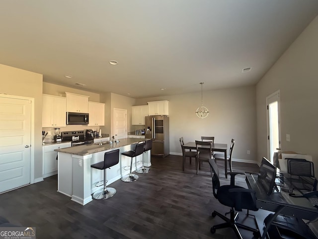 kitchen with white cabinets, appliances with stainless steel finishes, dark hardwood / wood-style flooring, and a center island with sink