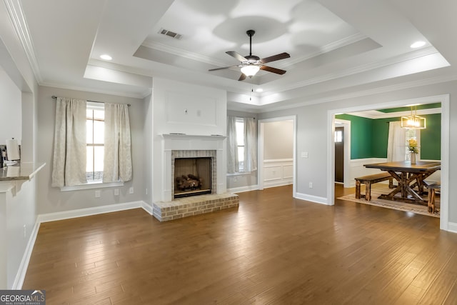 living room featuring dark hardwood / wood-style flooring, a brick fireplace, ornamental molding, a raised ceiling, and ceiling fan