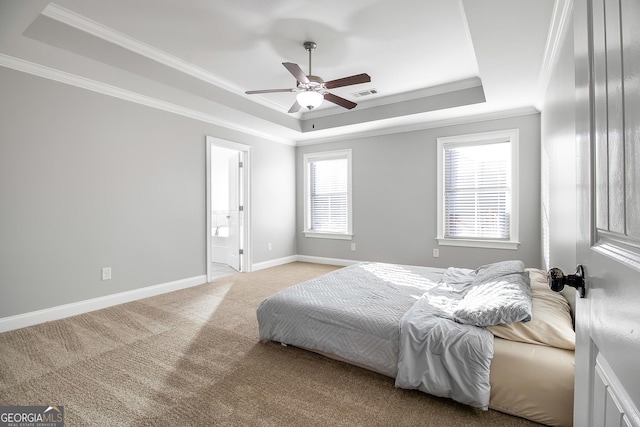 carpeted bedroom featuring a tray ceiling, ensuite bath, ceiling fan, and crown molding