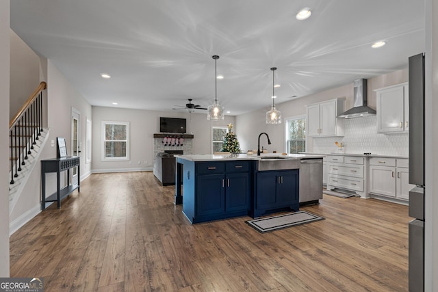 kitchen featuring a wealth of natural light, wall chimney range hood, blue cabinetry, white cabinetry, and an island with sink