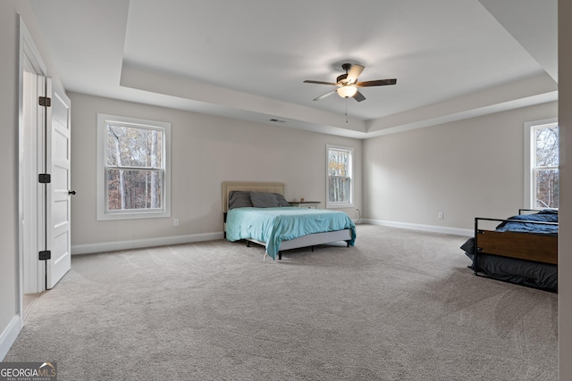 bedroom with a tray ceiling, multiple windows, ceiling fan, and light carpet