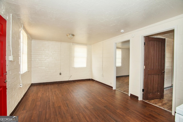 unfurnished room with crown molding, brick wall, dark wood-type flooring, and a textured ceiling