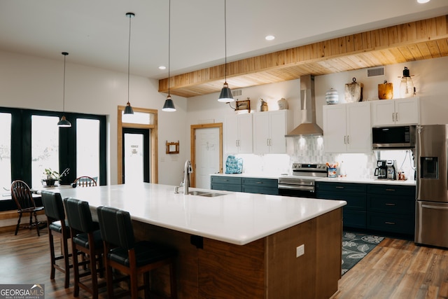 kitchen featuring white cabinets, wall chimney range hood, sink, hanging light fixtures, and stainless steel appliances