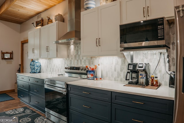 kitchen featuring dark wood-type flooring, white cabinets, wall chimney exhaust hood, tasteful backsplash, and stainless steel appliances