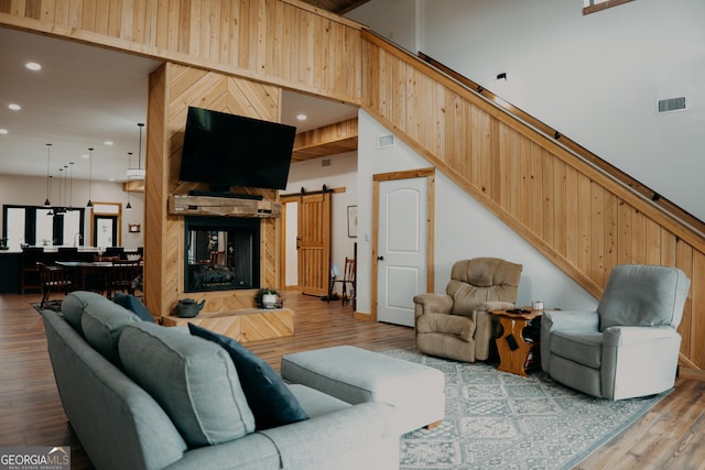 living room featuring a multi sided fireplace, a high ceiling, a barn door, and hardwood / wood-style flooring