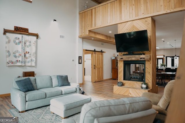 living room featuring a multi sided fireplace, a barn door, a towering ceiling, and wood-type flooring