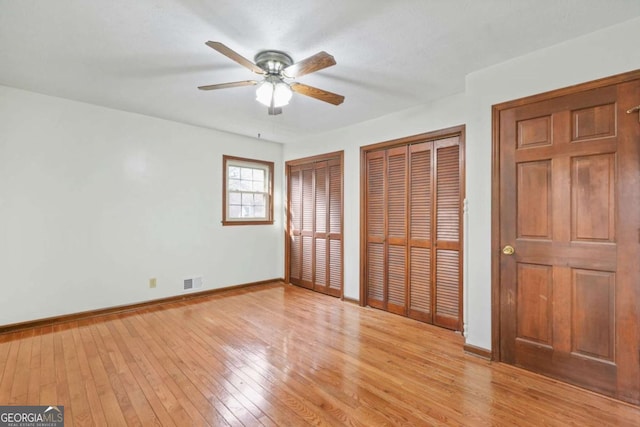 unfurnished bedroom featuring ceiling fan, two closets, and light wood-type flooring