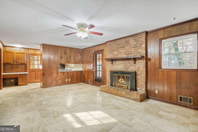 unfurnished living room with ceiling fan, wooden walls, and a brick fireplace