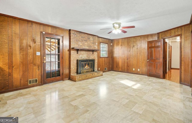 unfurnished living room featuring ceiling fan, wood walls, crown molding, a textured ceiling, and a fireplace