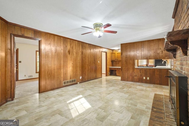 unfurnished living room featuring ceiling fan, wood walls, sink, and a brick fireplace