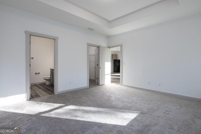 unfurnished bedroom featuring dark carpet, a spacious closet, and ensuite bath