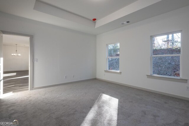 spare room with a raised ceiling, carpet floors, and an inviting chandelier