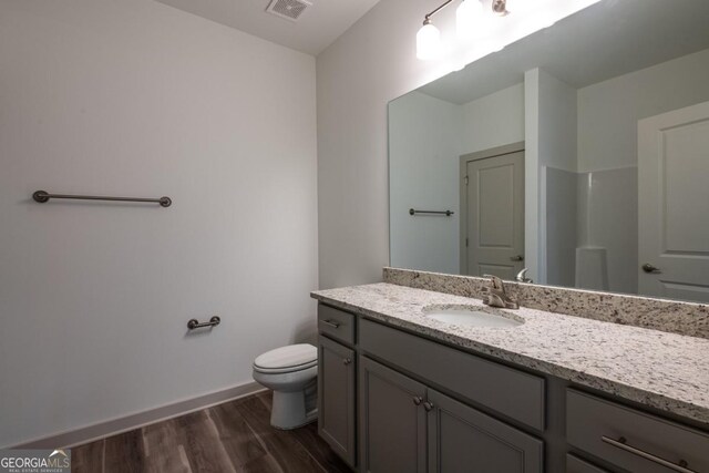 bathroom with walk in shower, hardwood / wood-style floors, vanity, and toilet